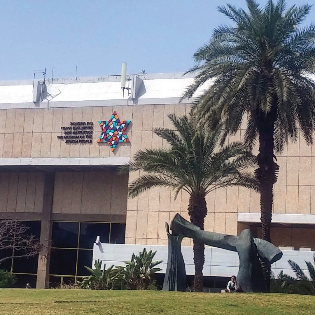 Stone facade of the ANU Museum building with a multicoloured Star of David emblem and palm trees