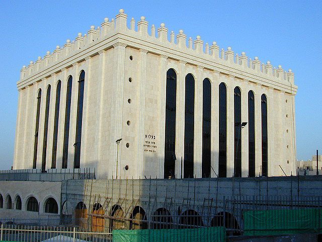 Exterior of the Belz Great Synagogue in Jerusalem, a large pale stone building with tall vertical windows.