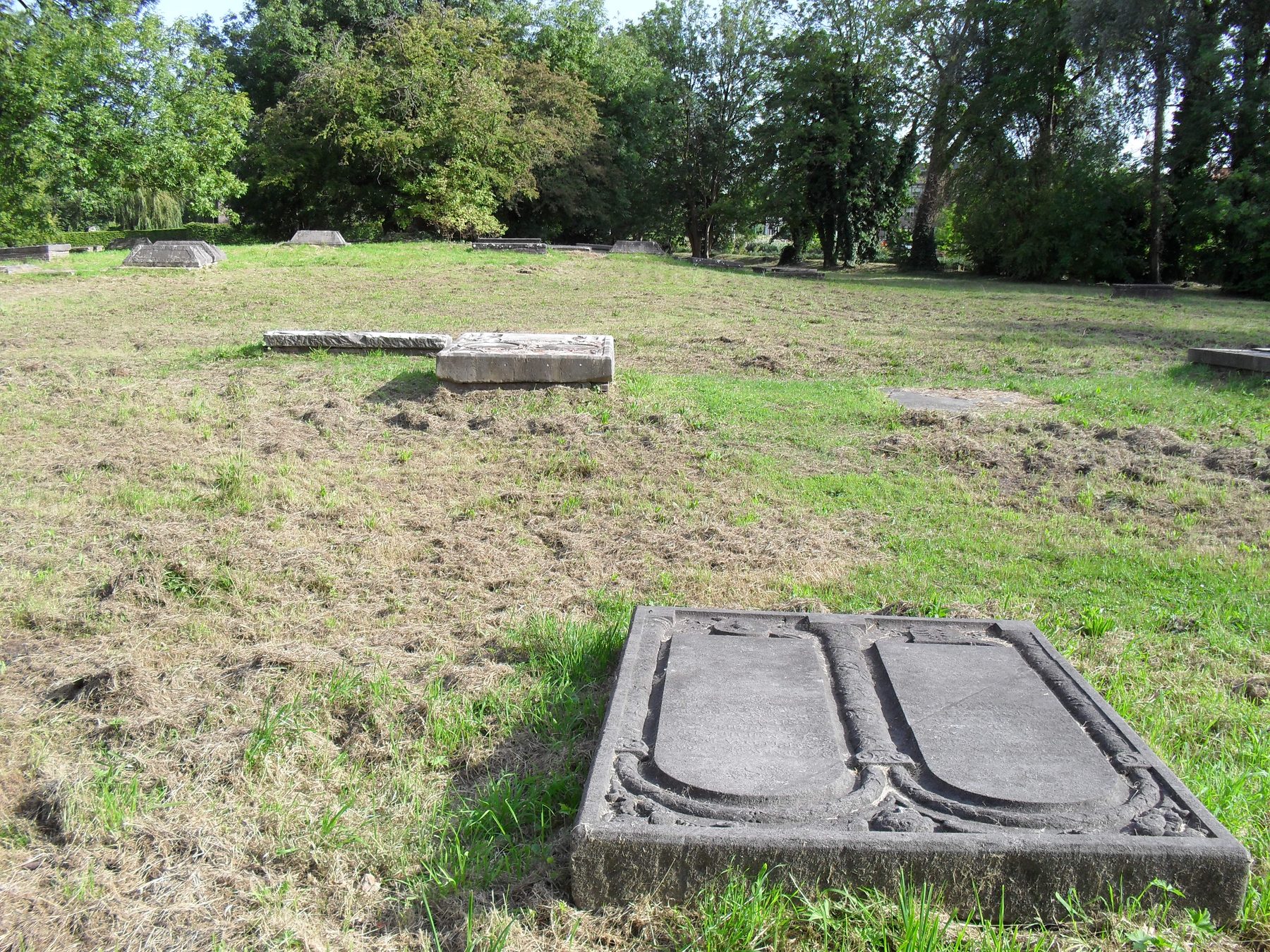 Carved Sephardi grave marker at Beth Haim cemetery, Ouderkerk aan de Amstel, with other stone tombs visible in the grass.