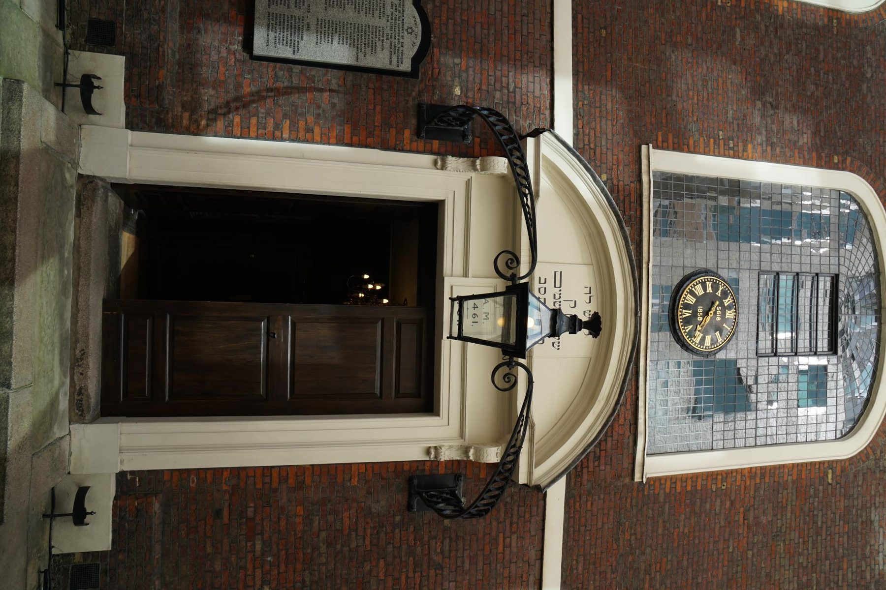 Entrance to Bevis Marks Synagogue, City of London - cream-coloured stone surround with dark wooden doors, red brick building facade, wrought-iron light bracket, and clock mounted above