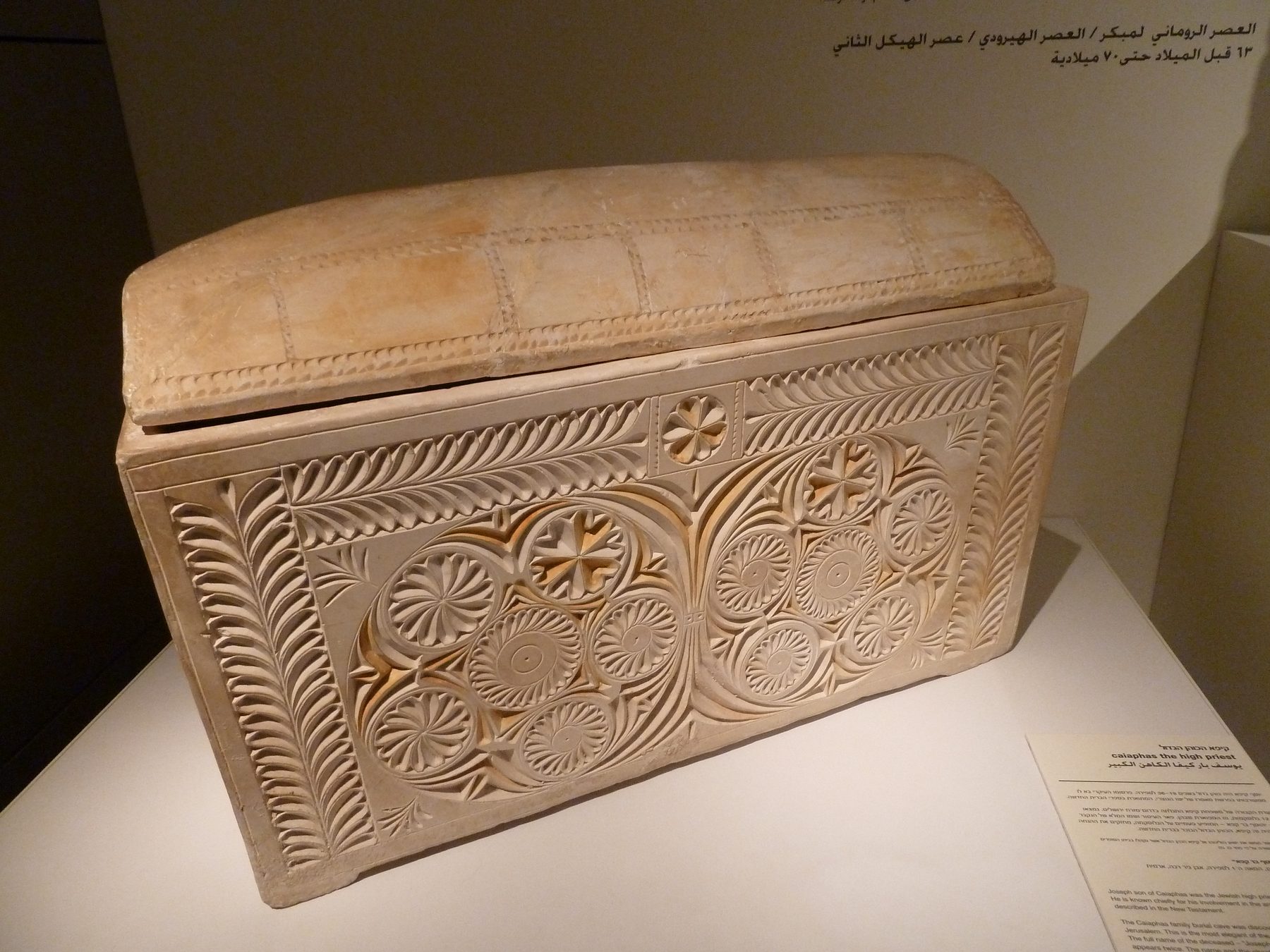 Ornate limestone ossuary carved with rosette medallions and leaf patterns, displayed in a museum case
