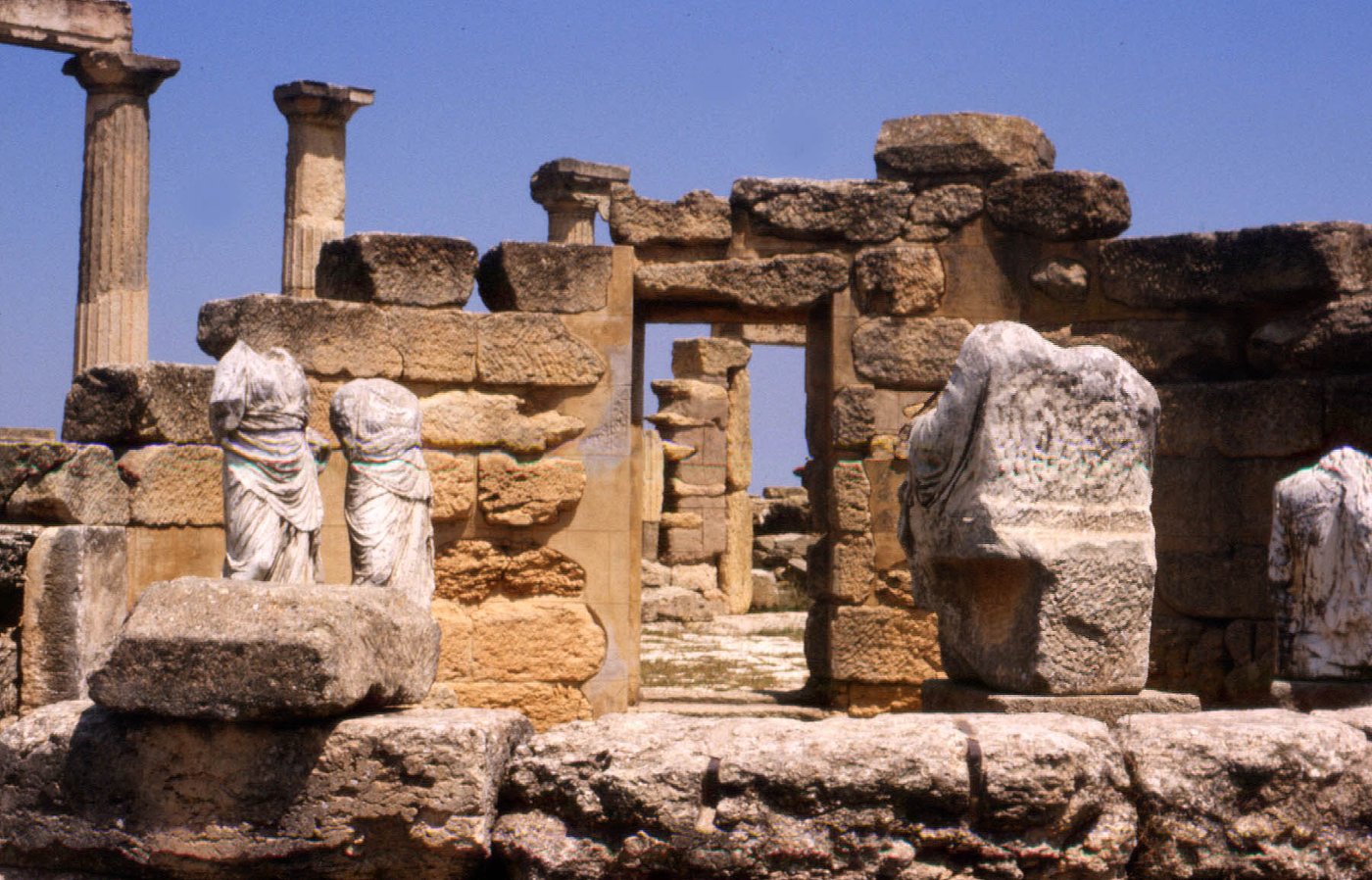 Standing stone columns and the ruined walls of an ancient Greek temple on a hillside.