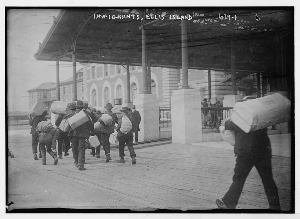 Immigrants at Ellis Island, New York, carrying suitcases and cloth-wrapped bundles of belongings