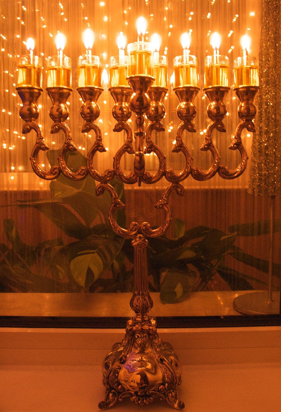 An ornate sterling-silver hanukkiah with all nine lights burning, standing on a window sill