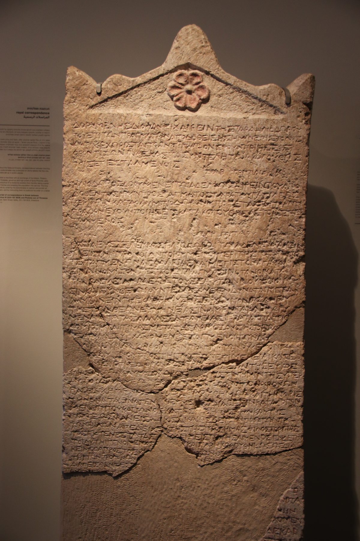 Limestone stele bearing Greek inscription with peaked top and flower relief