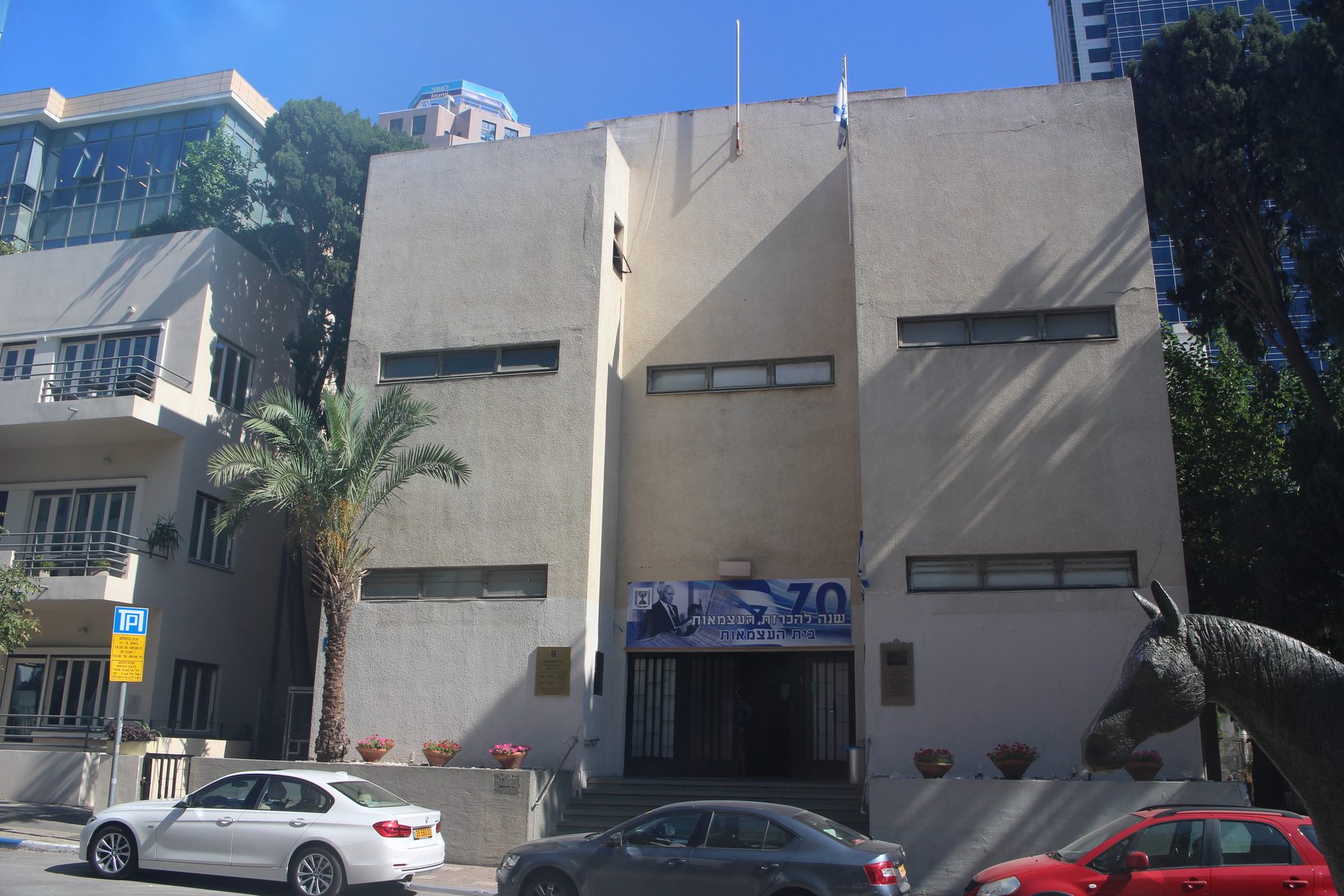 Modernist concrete exterior of Independence Hall Museum, 16 Rothschild Boulevard, Tel Aviv, with Israeli flags flying.