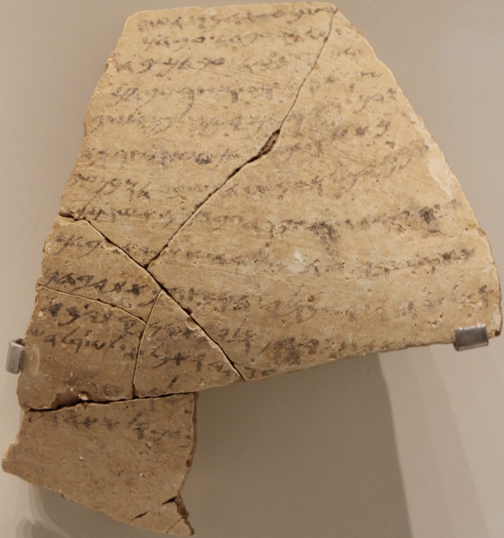 Pottery sherd inscribed with ancient Hebrew text, broken into several pieces, displayed in museum setting