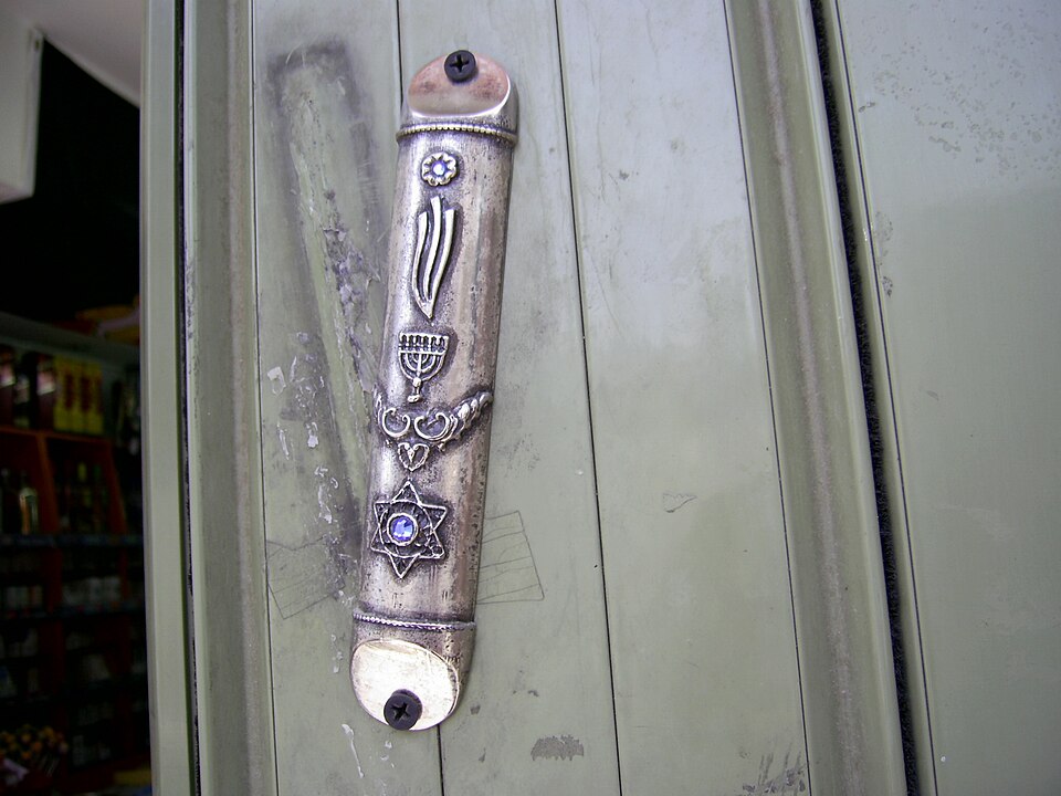 A decorative silver mezuzah case, set at a slant on a doorpost, embossed with a shin, a menorah and a Star of David