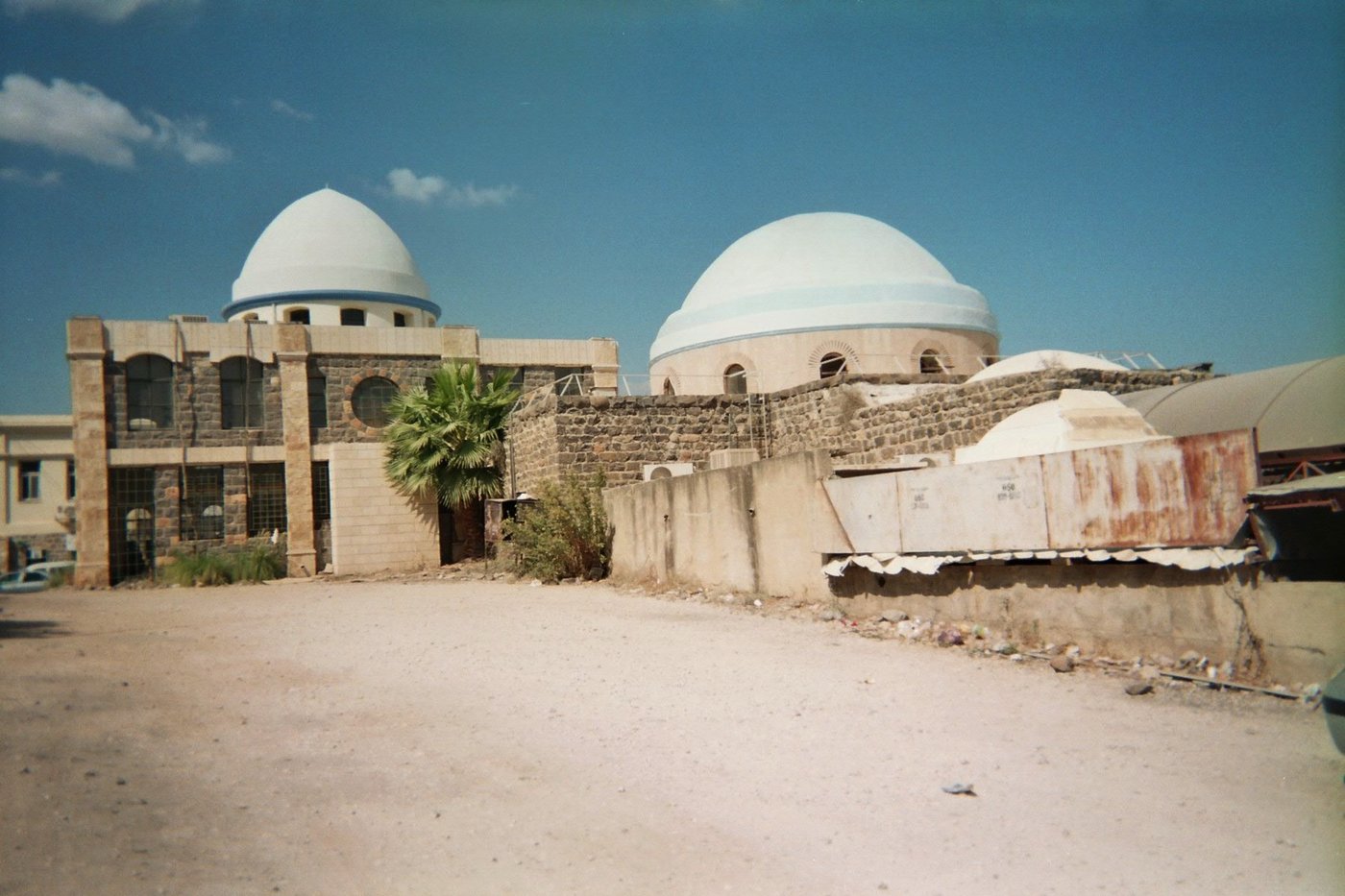 A white domed shrine and tower on a hillside above a lake.