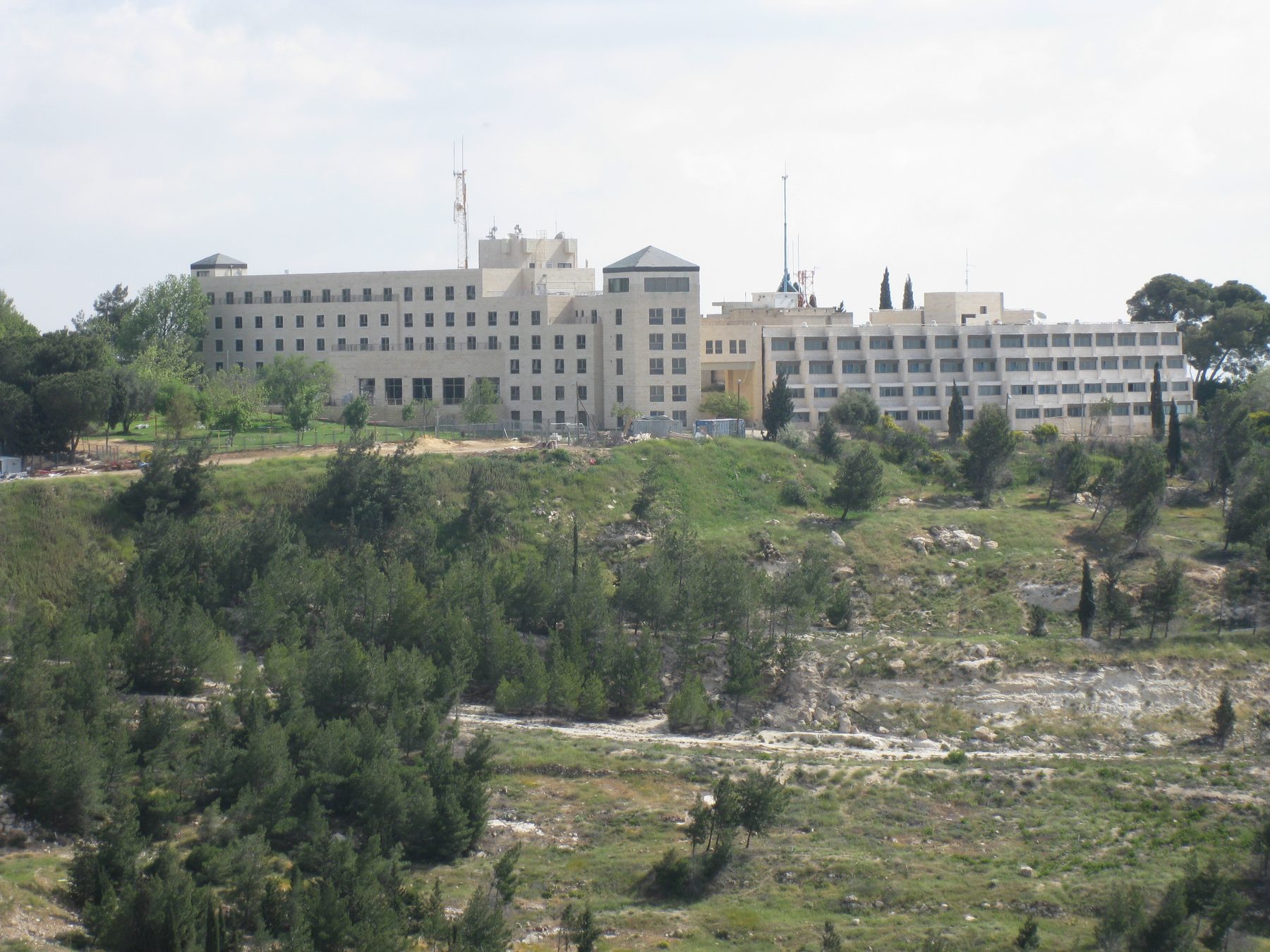 The Ramat Rahel archaeological site on a ridge south of Jerusalem, with modern kibbutz buildings built over ancient palace remains and Mediterranean vegetation on the slopes.