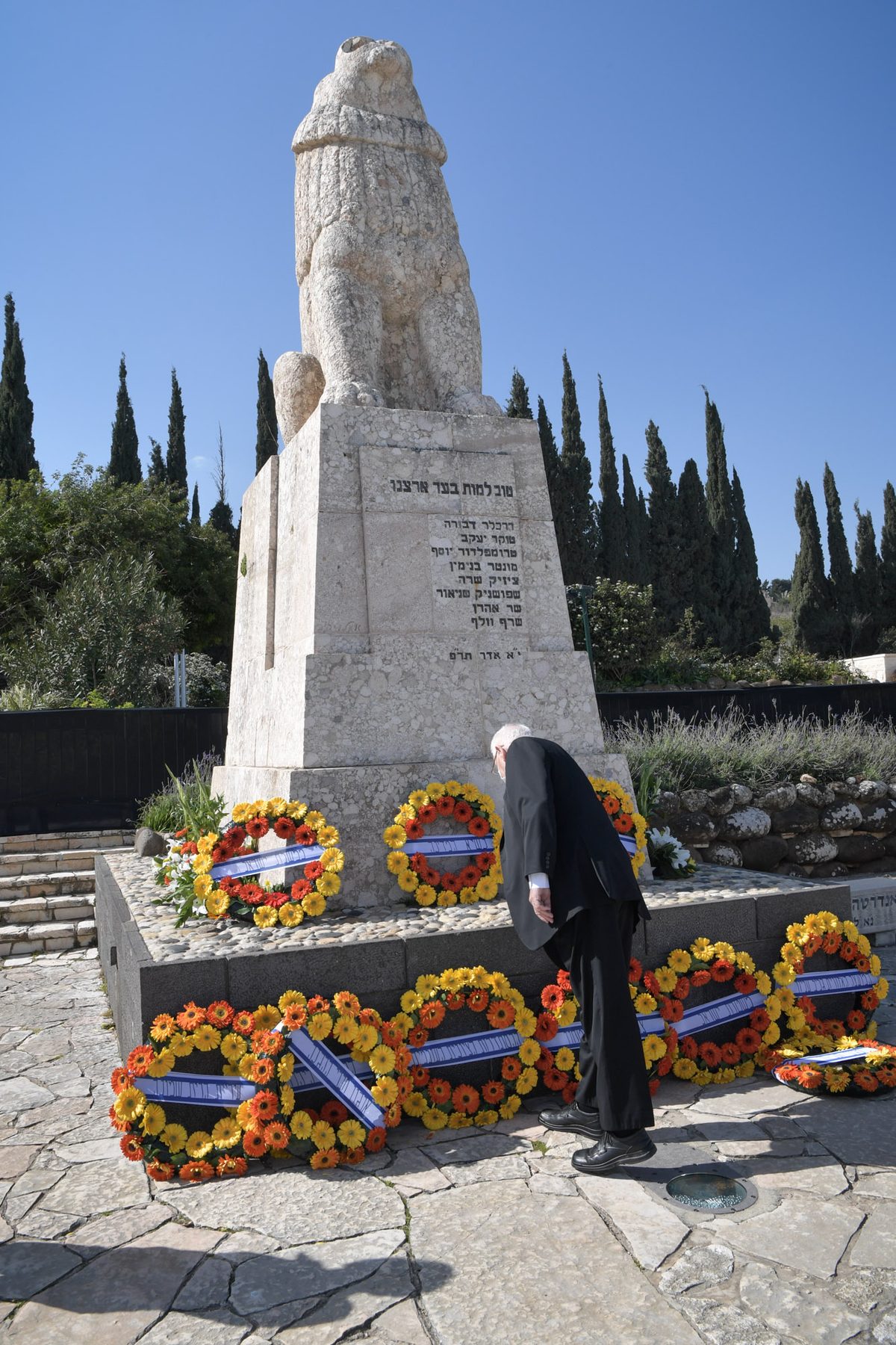 The roaring lion monument carved from basalt stone at Kfar Giladi cemetery, with memorial wreaths and Hebrew inscription plaque at the base