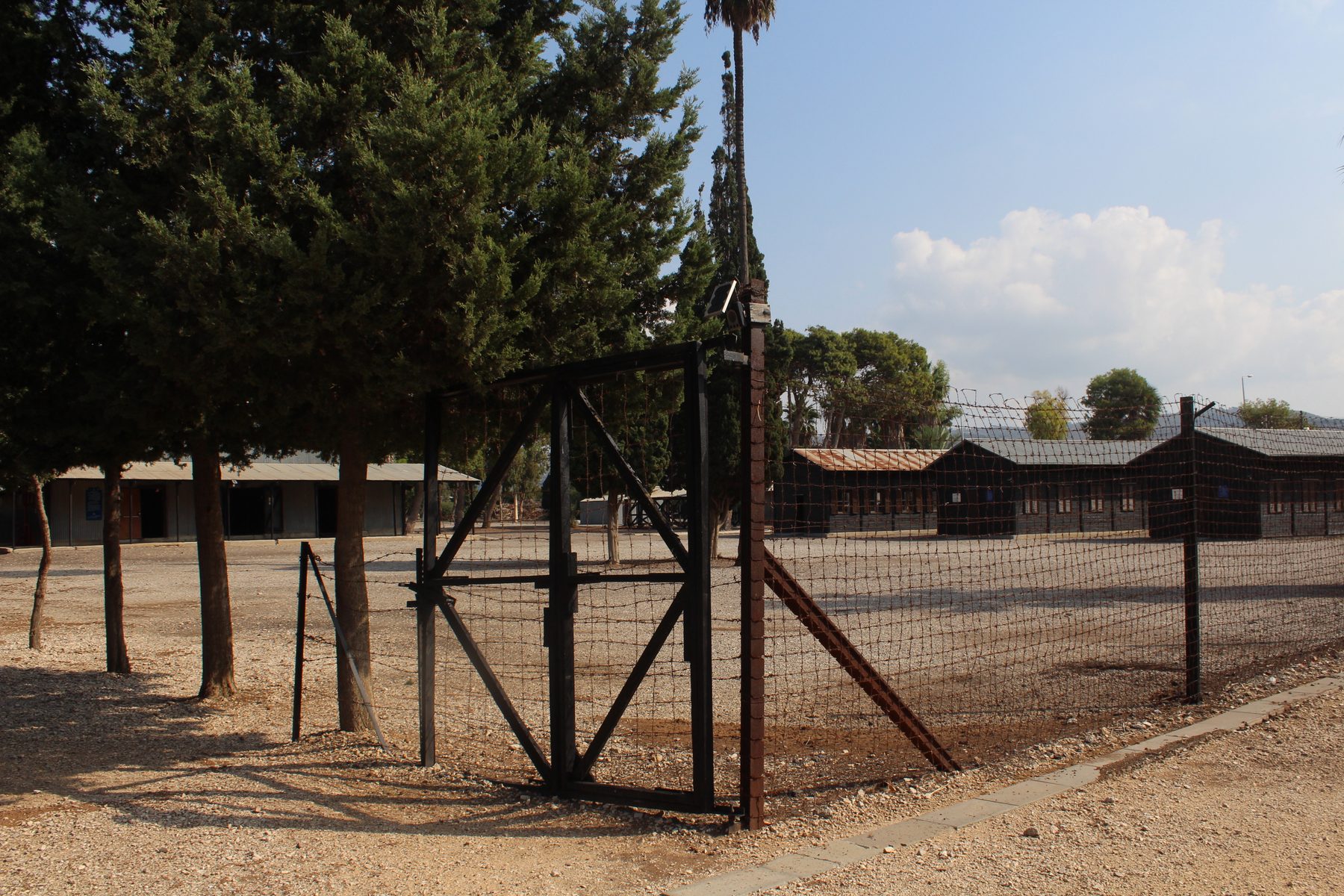 Barbed-wire fence and rustic brick barracks buildings of the Atlit detainee camp memorial site.