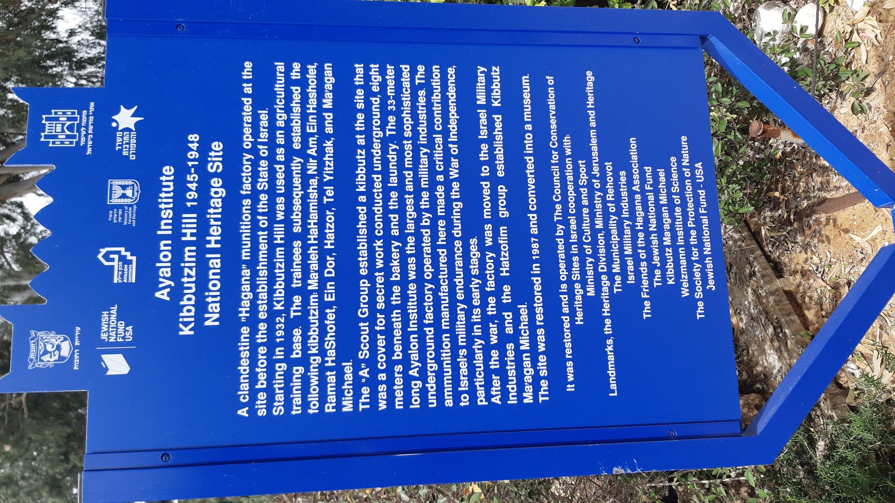 Blue heritage site marker at the Ayalon Institute, Rehovot, with historical text about the underground ammunition factory.