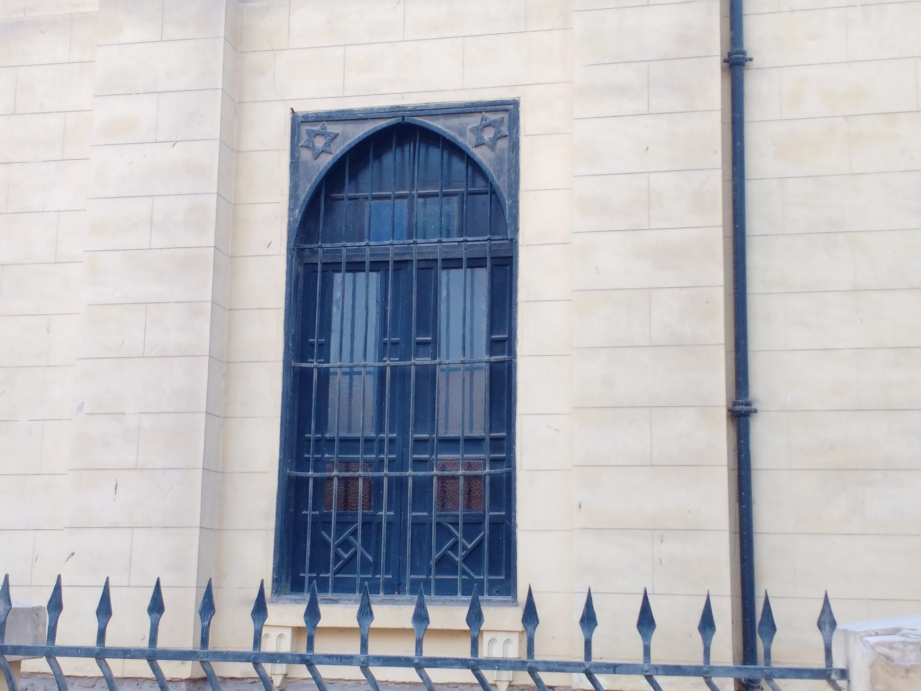 The entrance to the Ben Ezra Synagogue in Cairo: a blue arched door with Stars of David carved in the stone spandrel, set in white stone wall with decorative iron fence