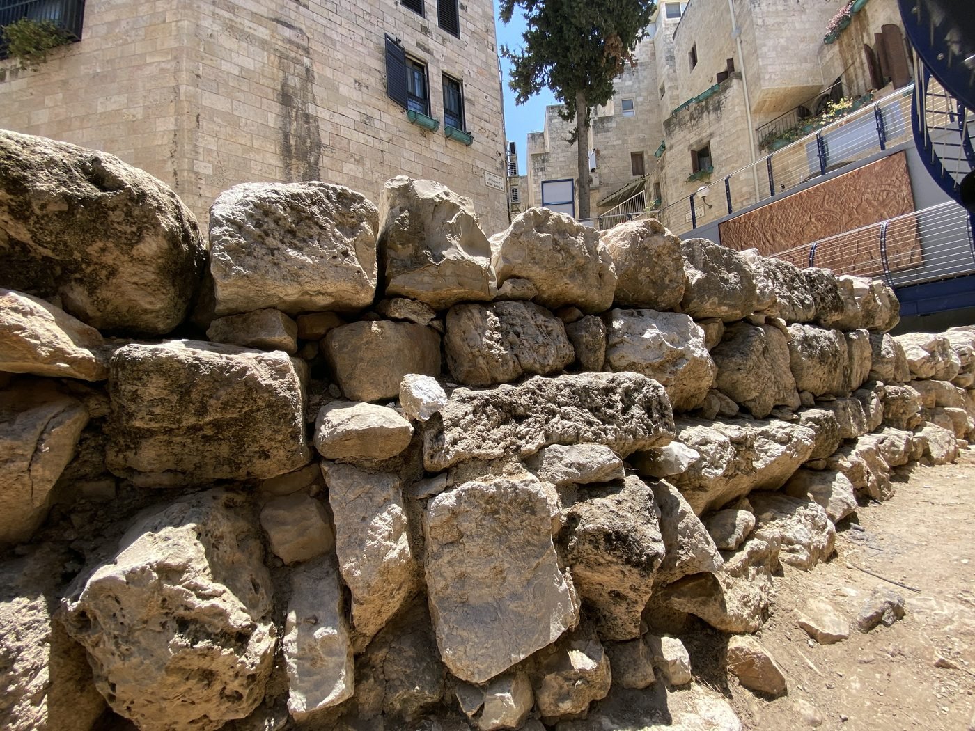 The exposed face of the Broad Wall (Hezekiah's Wide Wall) in the Jewish Quarter of Jerusalem: massive Iron Age ashlar stonework, roughly seven metres tall, visible at open-air street level with modern buildings rising behind it.