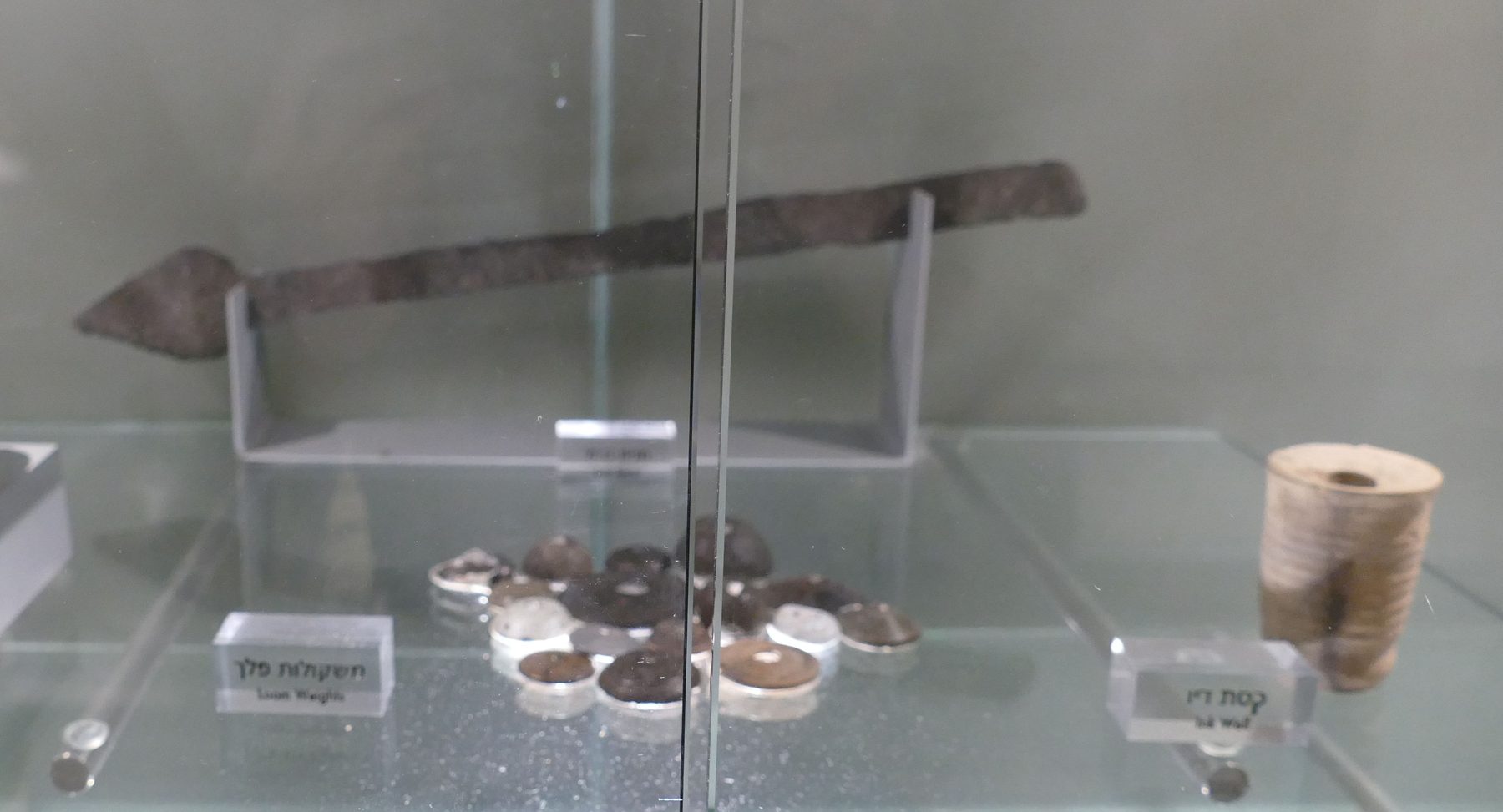 Museum display case of pottery vessels, a Roman iron spearhead, and stone weights from the Burnt House excavation, held at the Wohl Museum, Jerusalem.