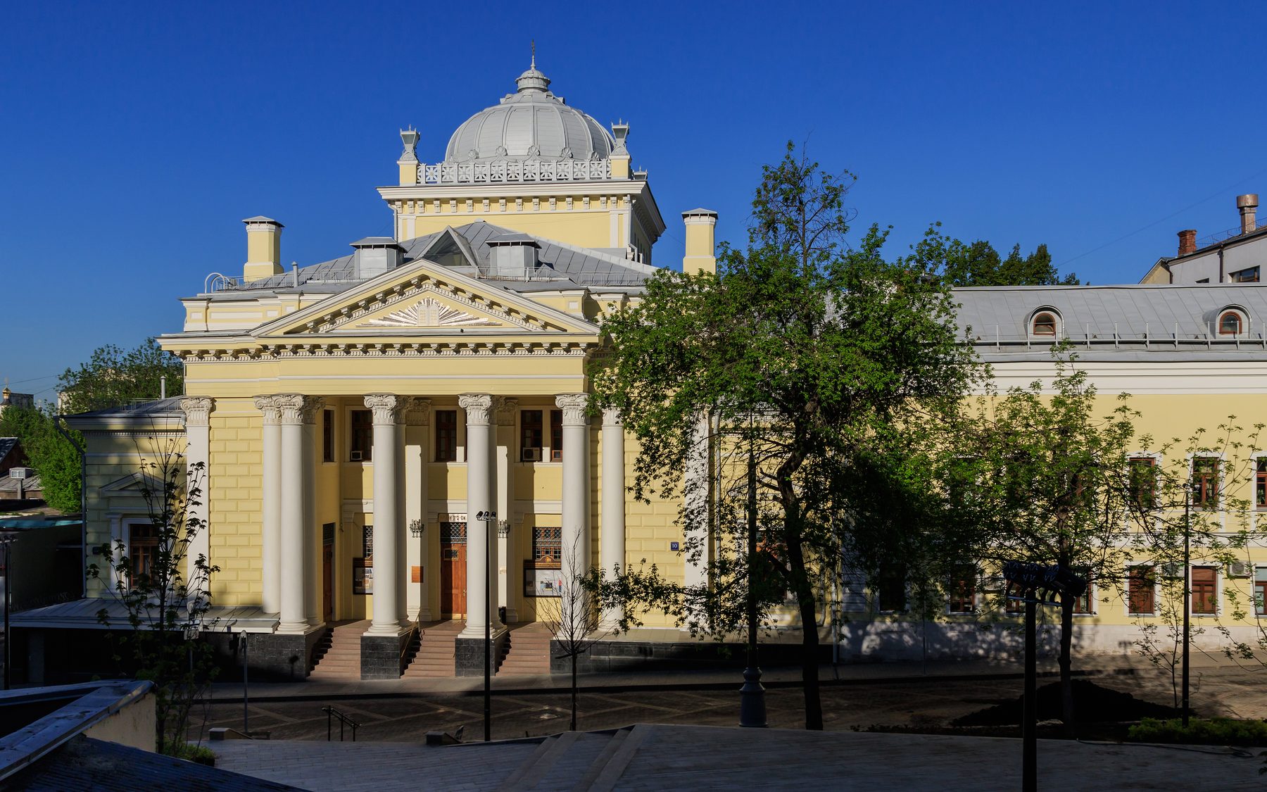 Cream-coloured neoclassical synagogue building with a distinctive dome and cupola, white columns at the entrance, and climbing ivy on the façade.