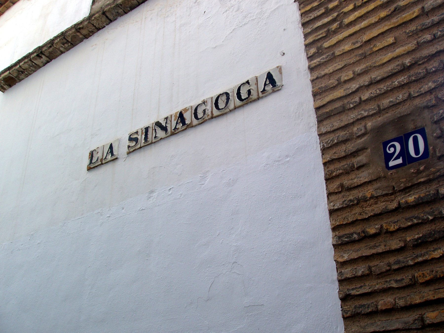 Exterior sign reading 'LA SINAGOGA' on the whitewashed wall of the Cordoba Synagogue, a fourteenth-century building in the medieval Jewish quarter.