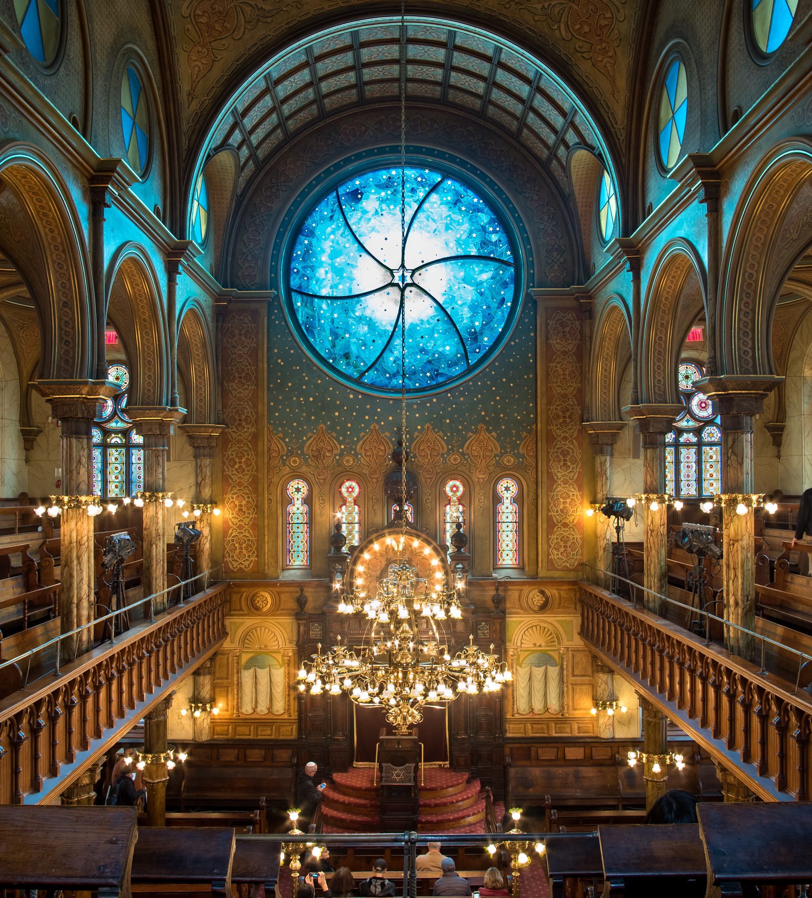 Interior of the Eldridge Street Synagogue sanctuary, showing Moorish Revival arches, stained glass windows, and brass chandeliers.