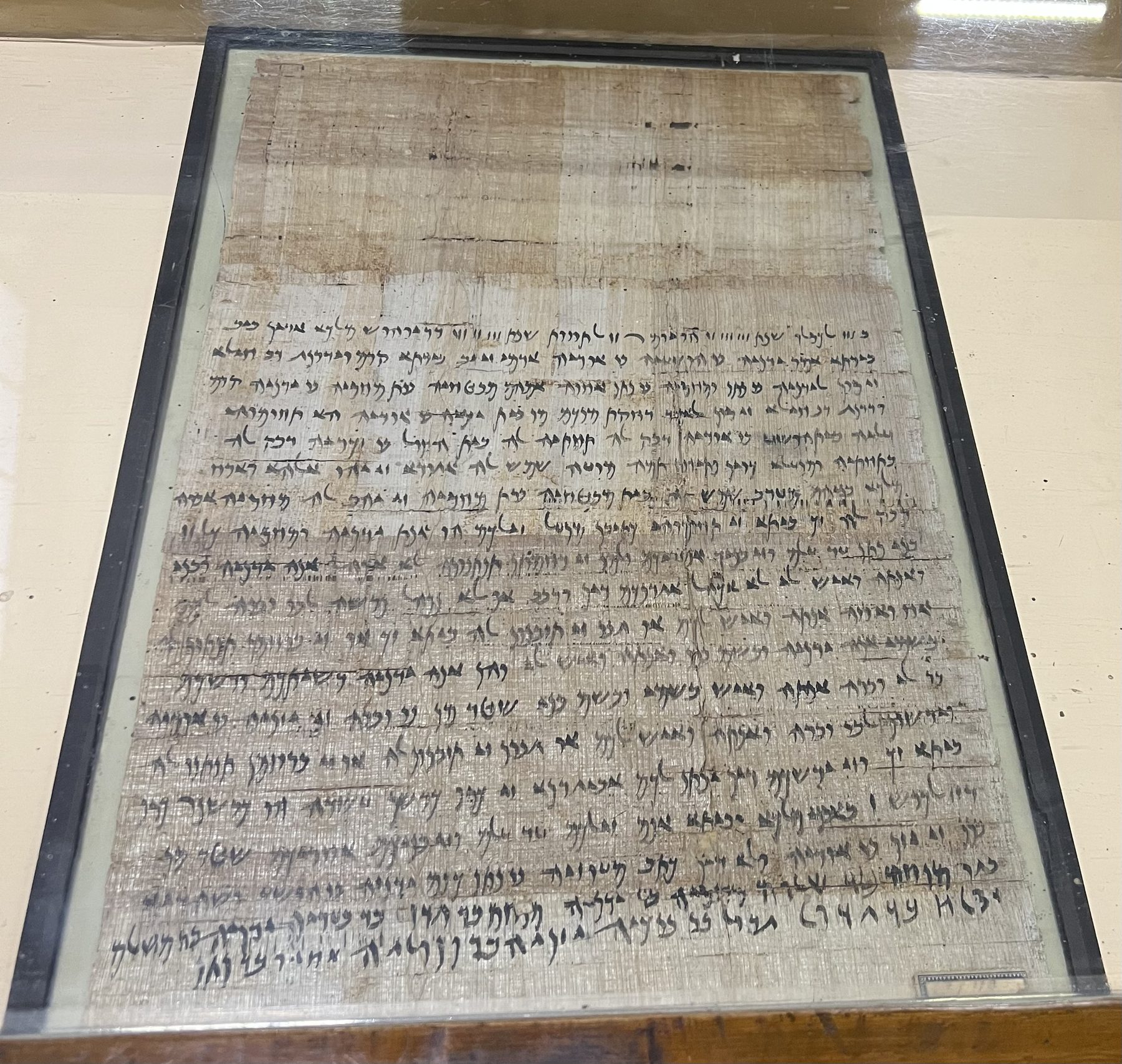 Ancient papyrus document with Hebrew text, displayed in a museum case under glass