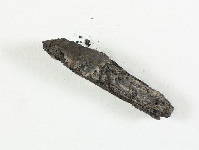 The charred remains of the En-Gedi scroll, a blackened carbonised parchment cylinder photographed against white background.