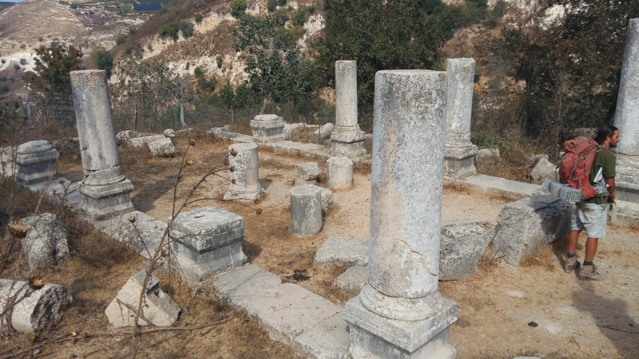 Standing basalt columns and dressed-stone remains of the ancient synagogue at Gush Halav, on a green Upper Galilee hillside.