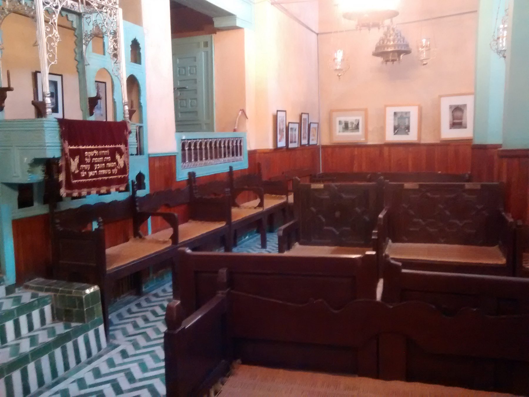 Interior of the Ibn Danan Synagogue showing the carved wooden ark, wooden pews, and geometric zellige tiled floor.