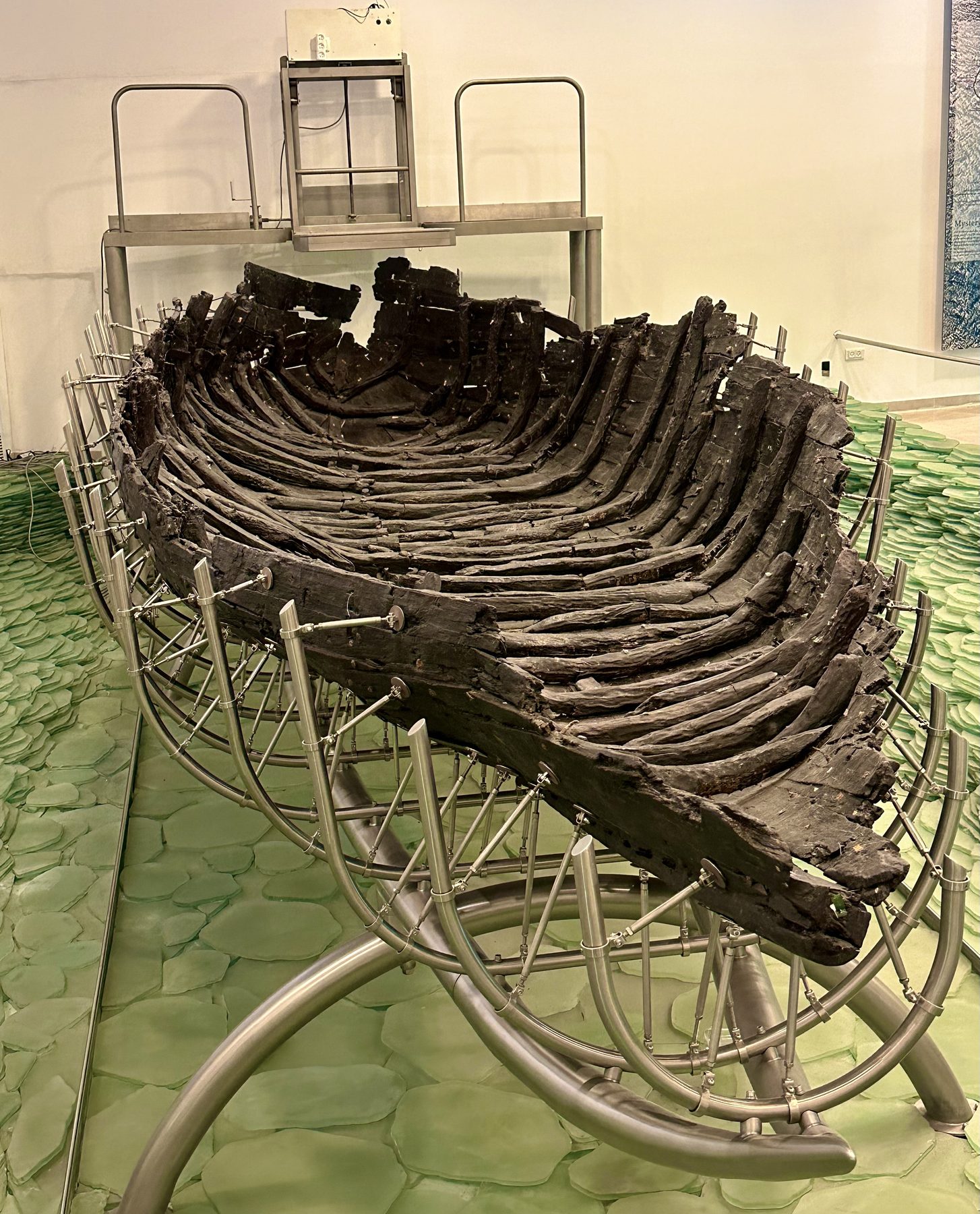The ancient wooden hull of the Magdala Boat displayed on museum support frames, showing ribbed construction and weathered timbers from repair patches