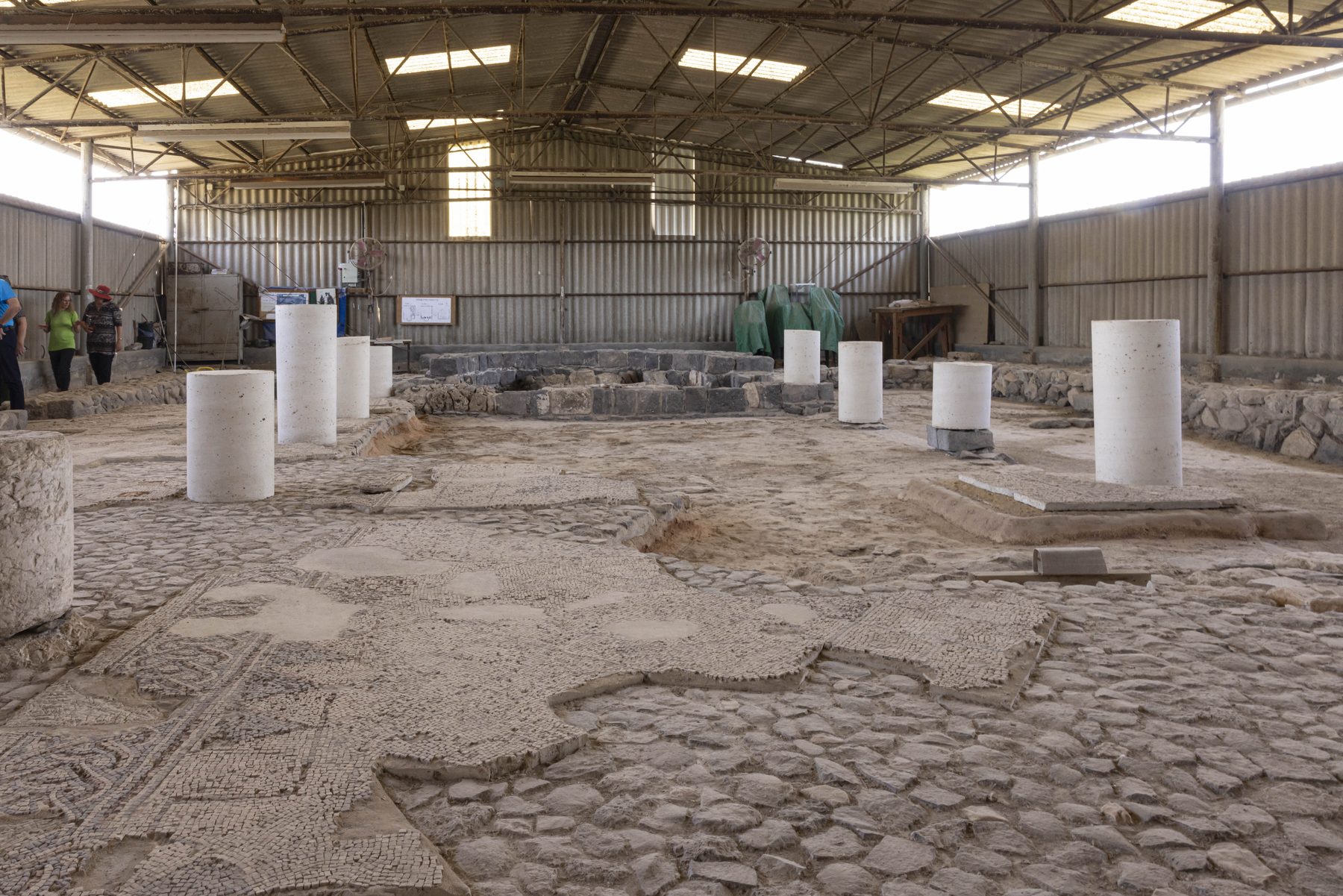 Excavated mosaic floors and stone foundations of the Maoz Haim synagogue, with protective modern shelter and layered archaeological remains visible.
