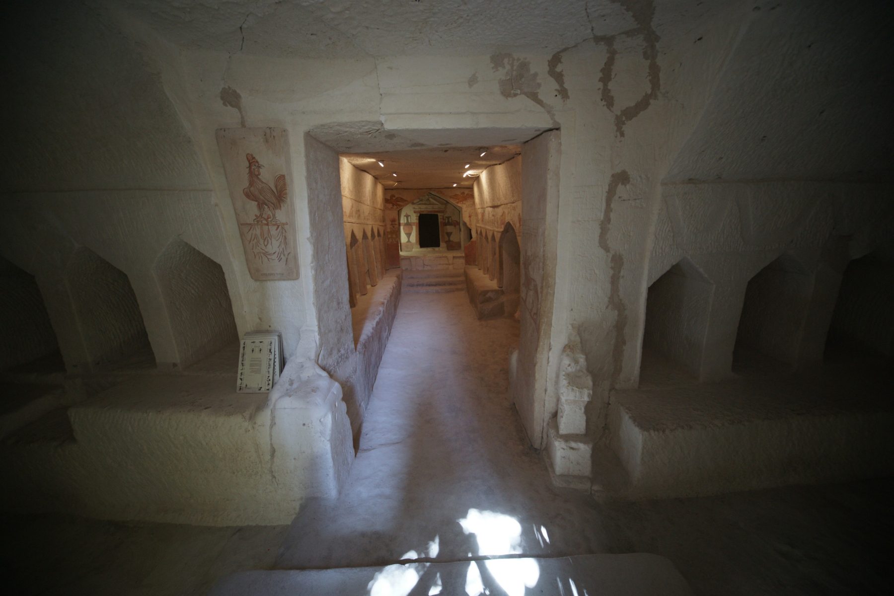 Interior of a carved burial chamber in the Maresha caves, showing arched burial niches (columbaria) flanking a central passage and painted frescoes on the walls