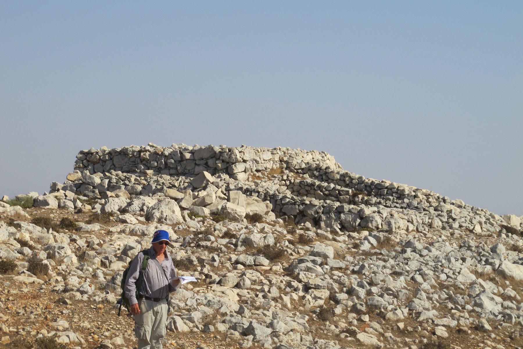 Rectangular stone structure on Mount Ebal with an archaeologist in hard hat examining the site