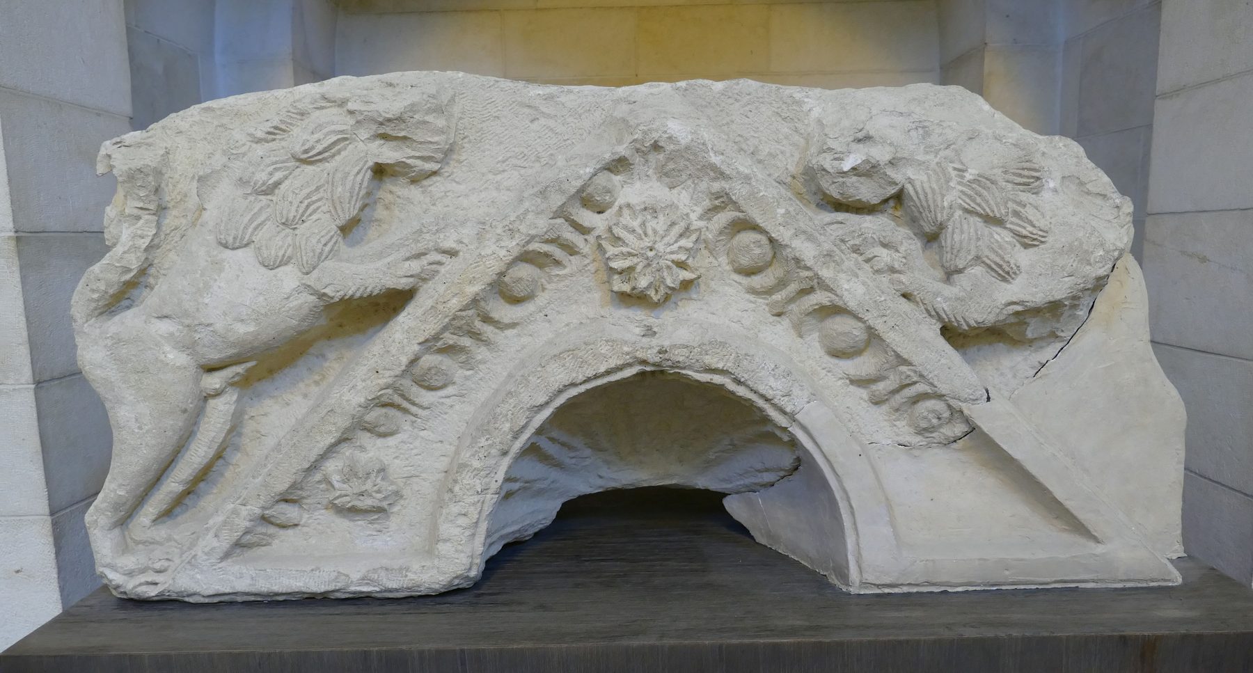 Carved stone Torah shrine lintel with gabled top and lions in relief, displayed in a museum case