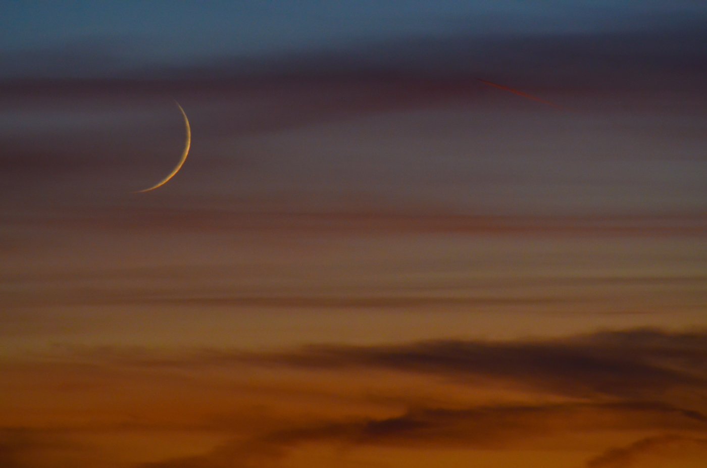 A slender crescent moon low in a deep blue twilight sky.