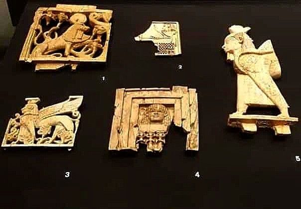 Museum display of carved ivory plaques from Nimrud, showing winged figures, horses, and decorative panels