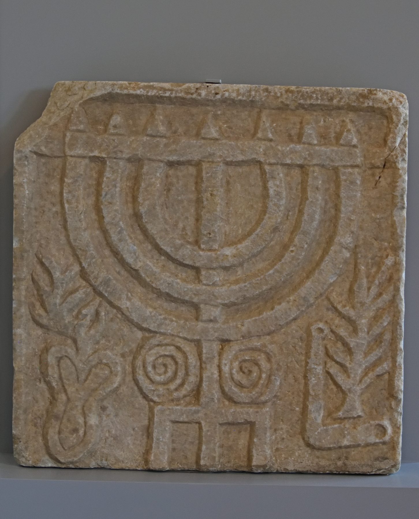 Carved stone relief of a seven-branched menorah with decorative spiral patterns and inscribed detail