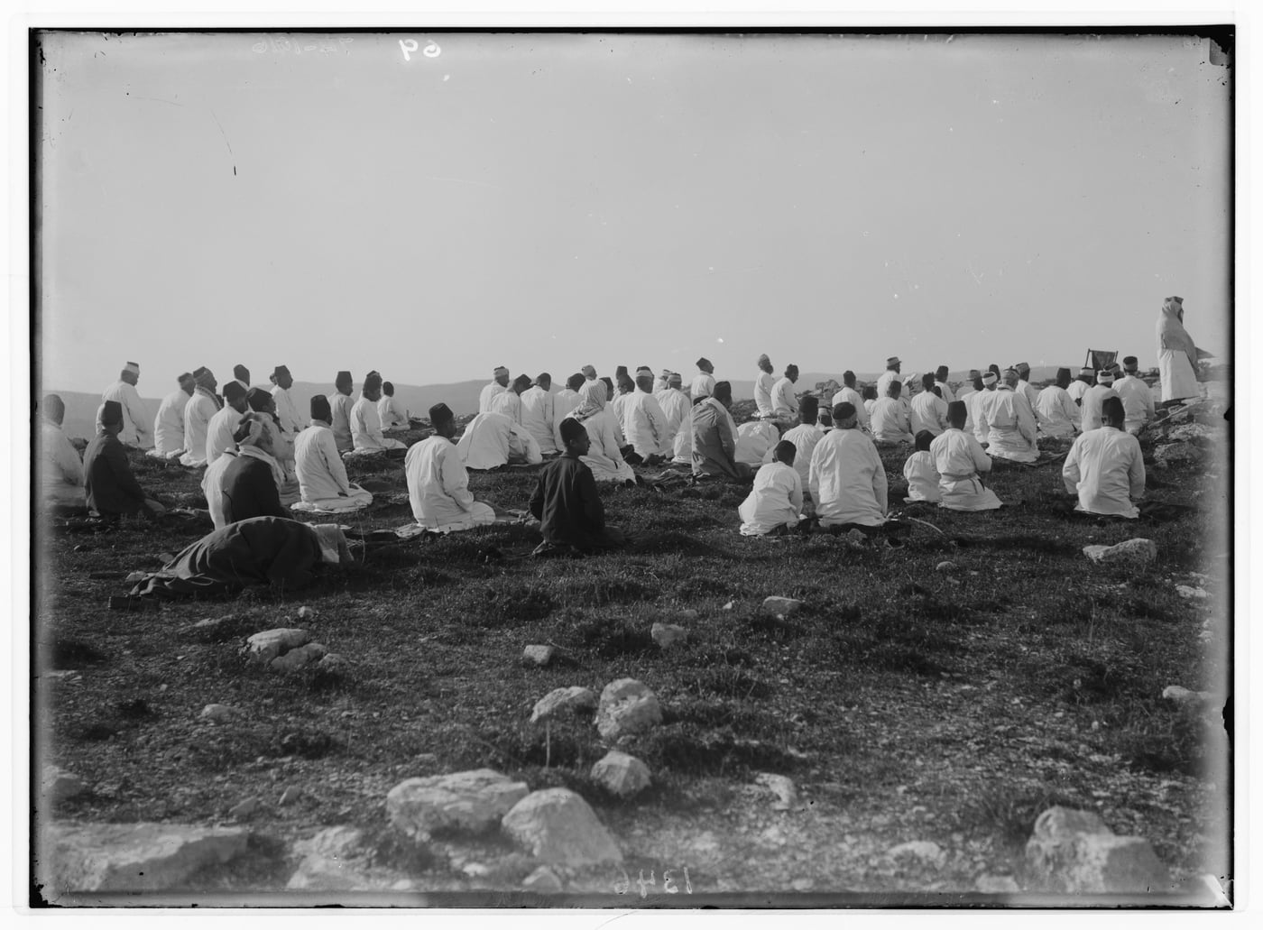 Black-and-white photograph of Samaritans in white robes kneeling in prayer on the open rocky summit of Mount Gerizim, around 1900.