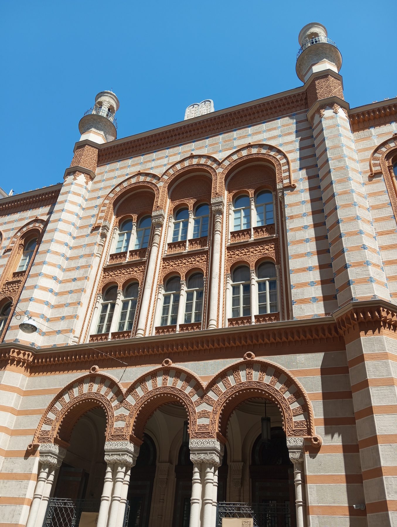 The Rumbach Street Synagogue facade, showing twin towers with onion domes and horseshoe-arched windows in red brick with white stone banding.