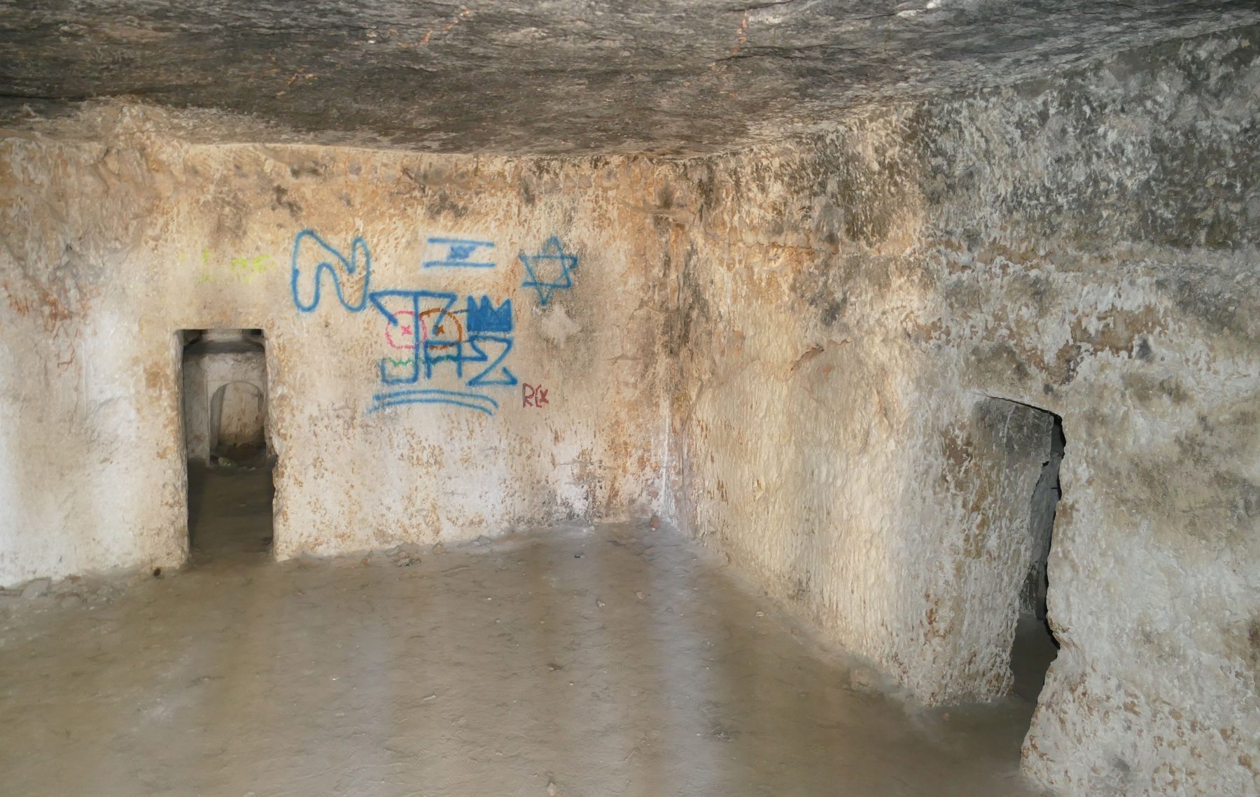 Rock-cut underground chamber of the Sanhedria Tombs with stone walls and low doorways connecting interior burial chambers.