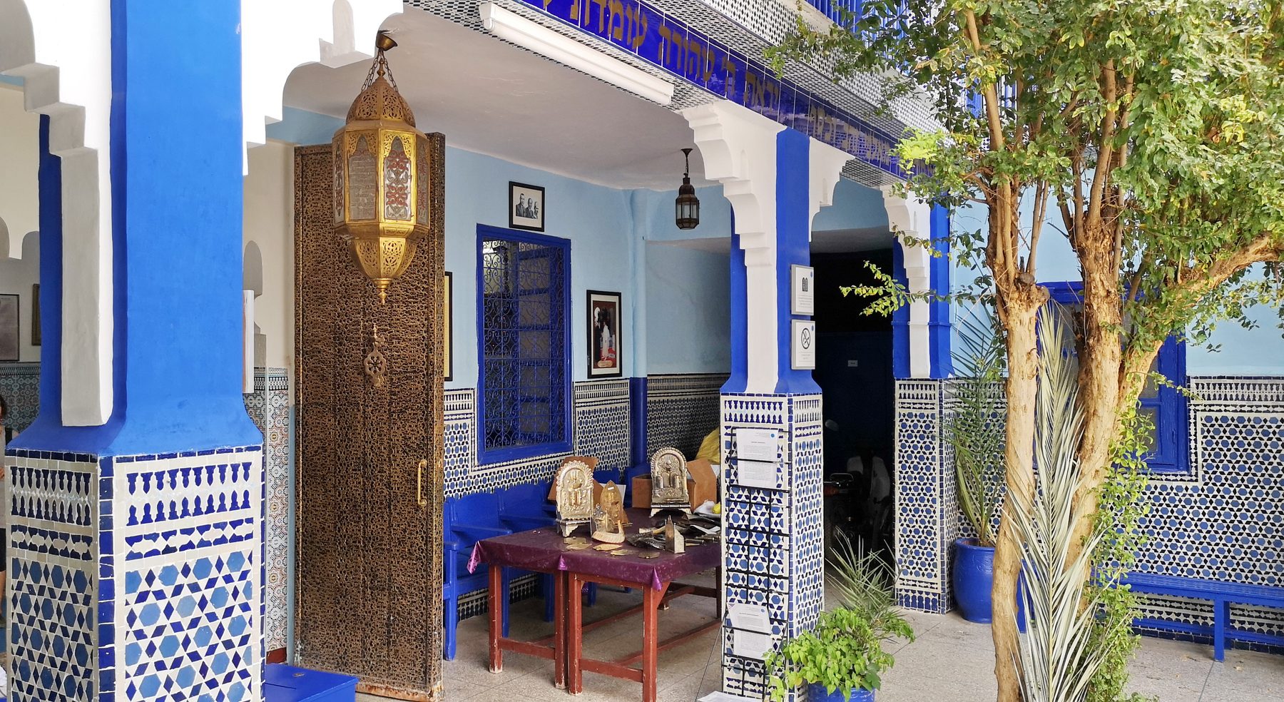 Interior courtyard of the Slat al-Azama with brilliant blue walls, ornate brass lantern, geometric zellige tilework, and arched white ceilings