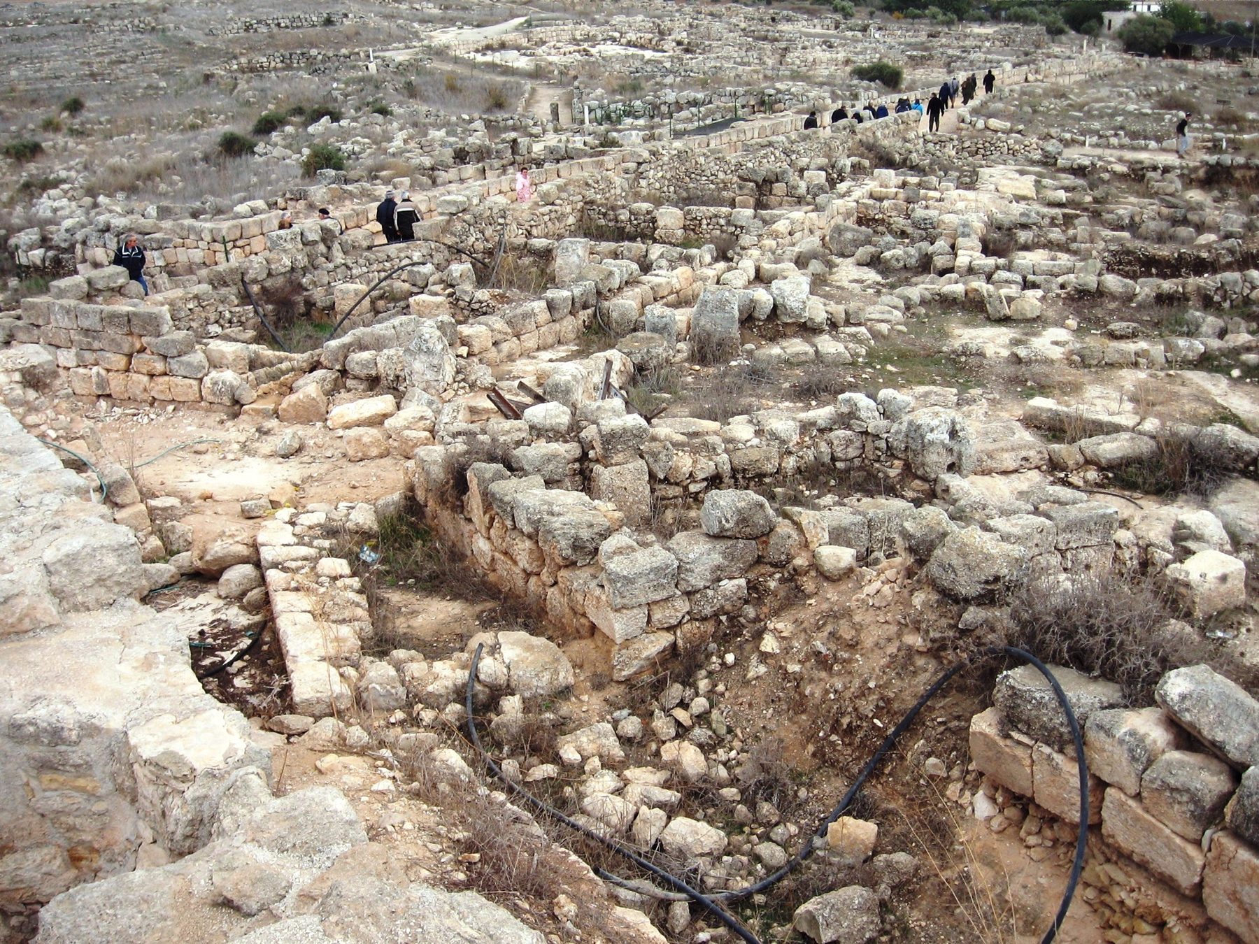 Stone foundations, paved floor and bimah of the Susiya Synagogue, with visitors at the archaeological site in the southern Hebron hills.