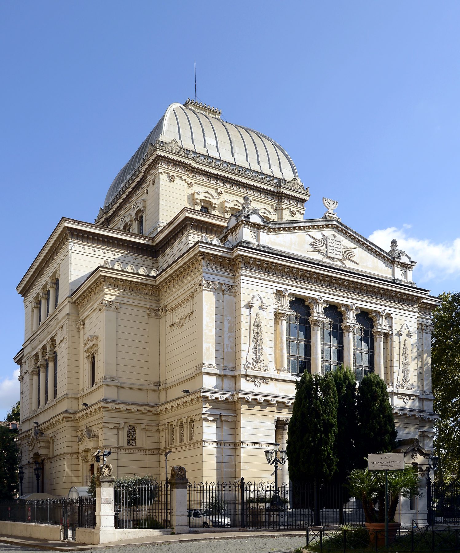 Exterior of the Tempio Maggiore with its distinctive square aluminium dome, neoclassical facade with tall arched windows, ornamental details, and a Star of David on the roof.