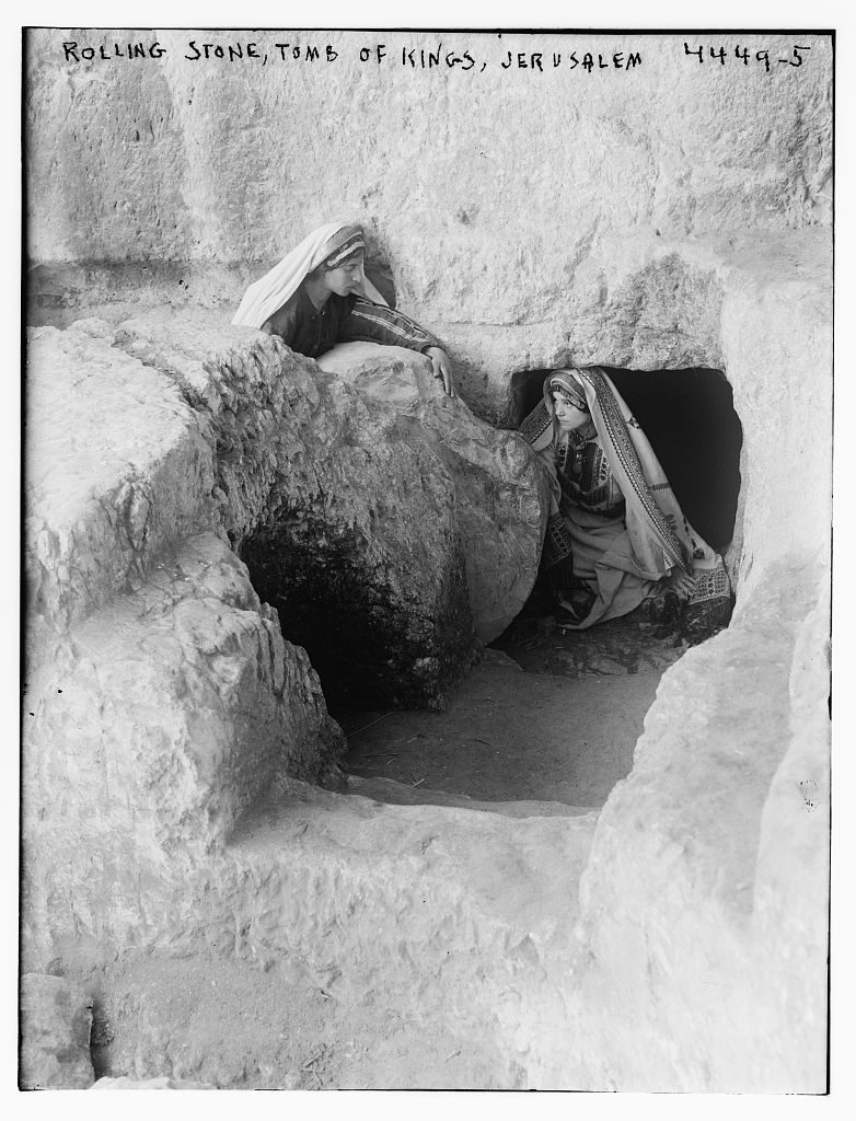 Rolling stone at the entrance to the Tomb of the Kings, Jerusalem - a large circular disc of carved stone sitting in its original groove, with two figures examining it.