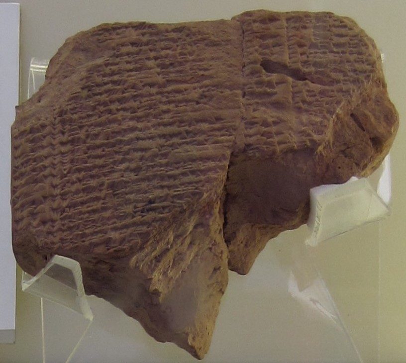 A clay tablet fragment bearing dense cuneiform inscriptions on multiple faces, photographed at an angle against a neutral background